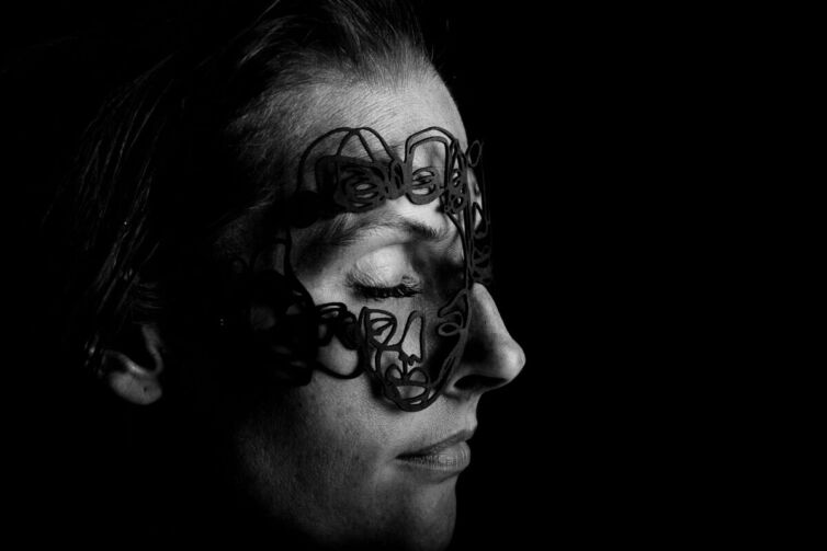 Black and white portrait of a person wearing a lace mask over their eyes and forehead.