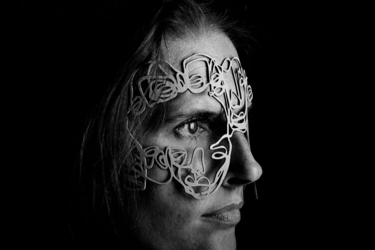 Black and white portrait of a person wearing a lace mask that covers part of the face.
