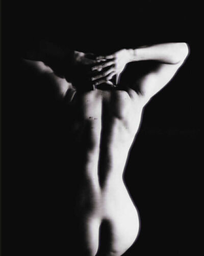 Black and white image of a human figure from the back with arms raised and hands on the head.