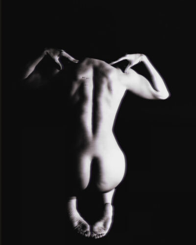 Black and white image of a human figure with a focus on the back and arms positioned near the head.