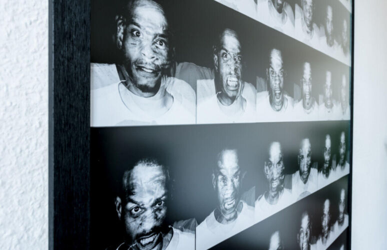 Collage of black and white portraits displaying various facial expressions on a wall.