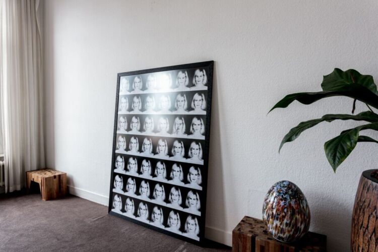 Framed artwork featuring a grid of black and white portraits displayed against a wall.