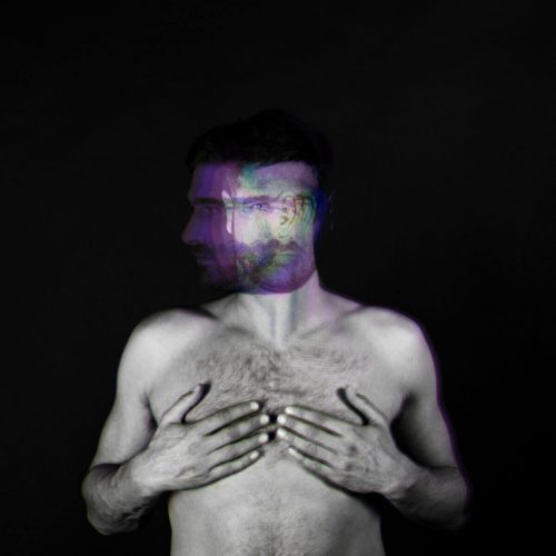 Black and white portrait of a man with a double exposure effect, showing a blurred face and hands on his chest.