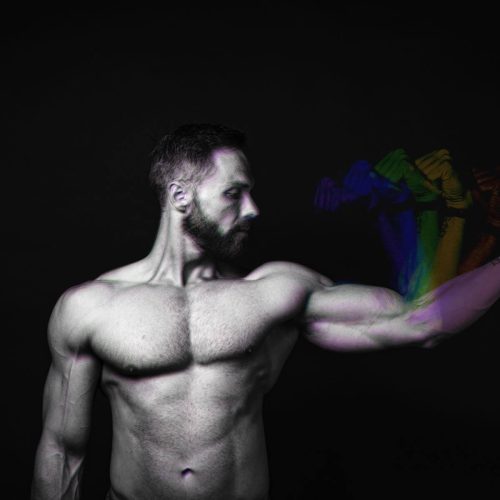 A muscular man flexing his arm with colorful effects in a black and white image.