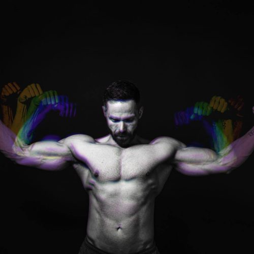 A muscular man flexing his arms with a black background and colorful hand shadows.